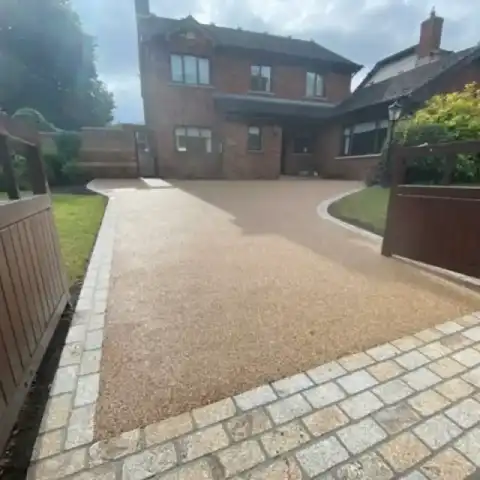 A two-story brick house with a newly finished resin-bound driveway, bordered by stone blocks and wooden gates, on a cloudy day.